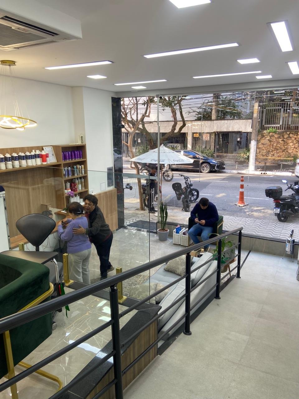 Ambiente do salão com poltronas verdes, detalhes dourados e vista para a rua