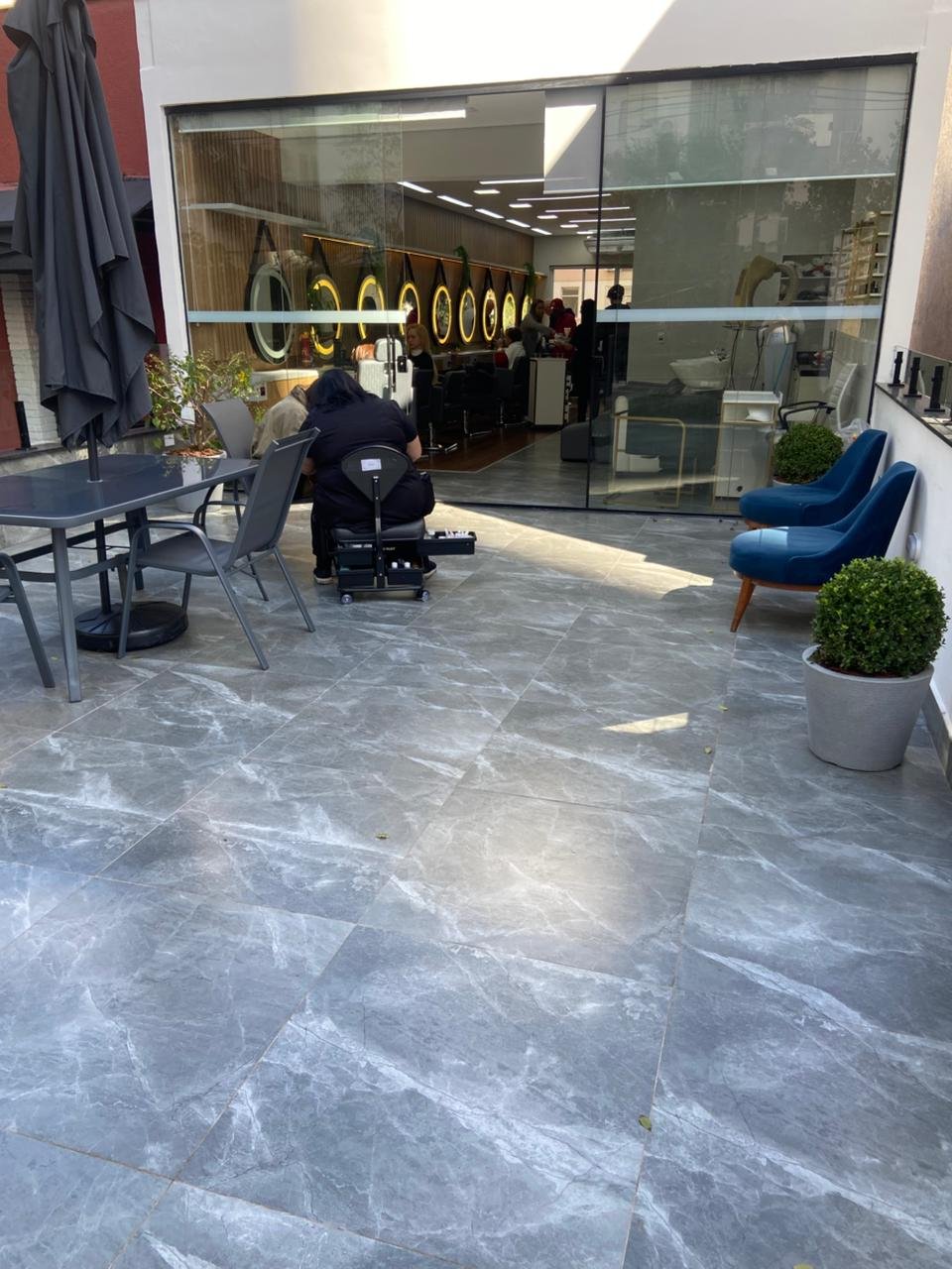 Varanda externa com piso de mármore, poltronas azuis e vasos de plantas